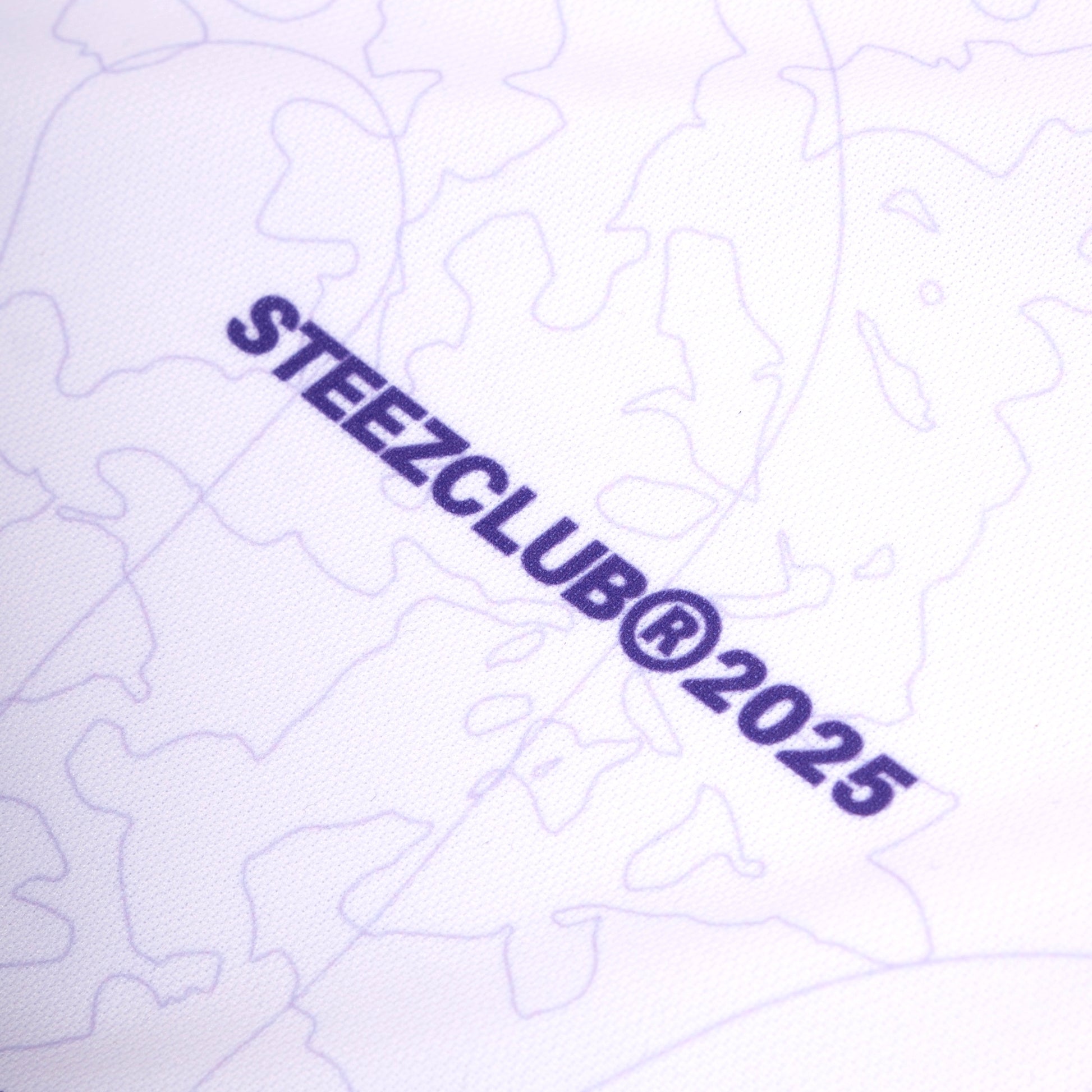 Gros plan sur un tissu blanc avec un motif subtil en lignes fines de couleurs violette. On y voit le texte "STEEZCLUB® 2025" imprimé en violet foncé, légèrement incliné. L'arrière-plan présente un motif abstrait de formes organiques et courbes.