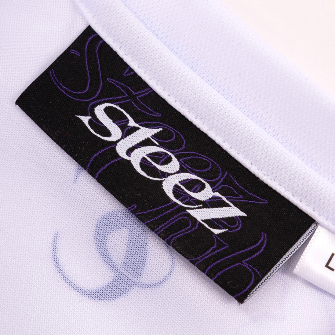 Etiquette de col du maillot Steez Club - Marque brodée sur fond noir avec détails violets, offrants une finition premium et un style streetwear authentique
