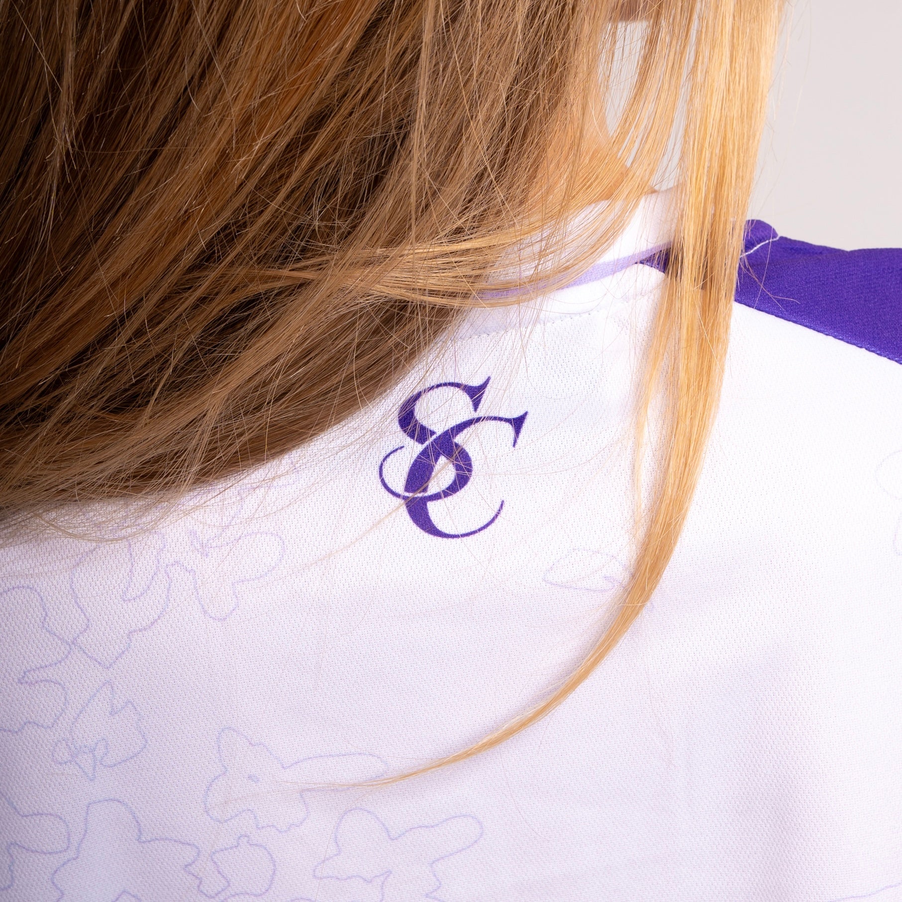 Détail du col arrière du maillot Steez Club - Logo SC imprimé en violet sur tissu blanc avec motifs subtils. Une finition élégante pour un look streetwear unique.